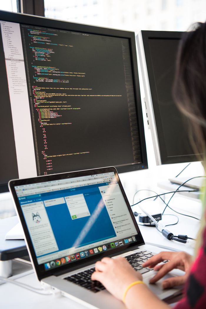 About Programmer working on code across multiple screens in a modern office setting.